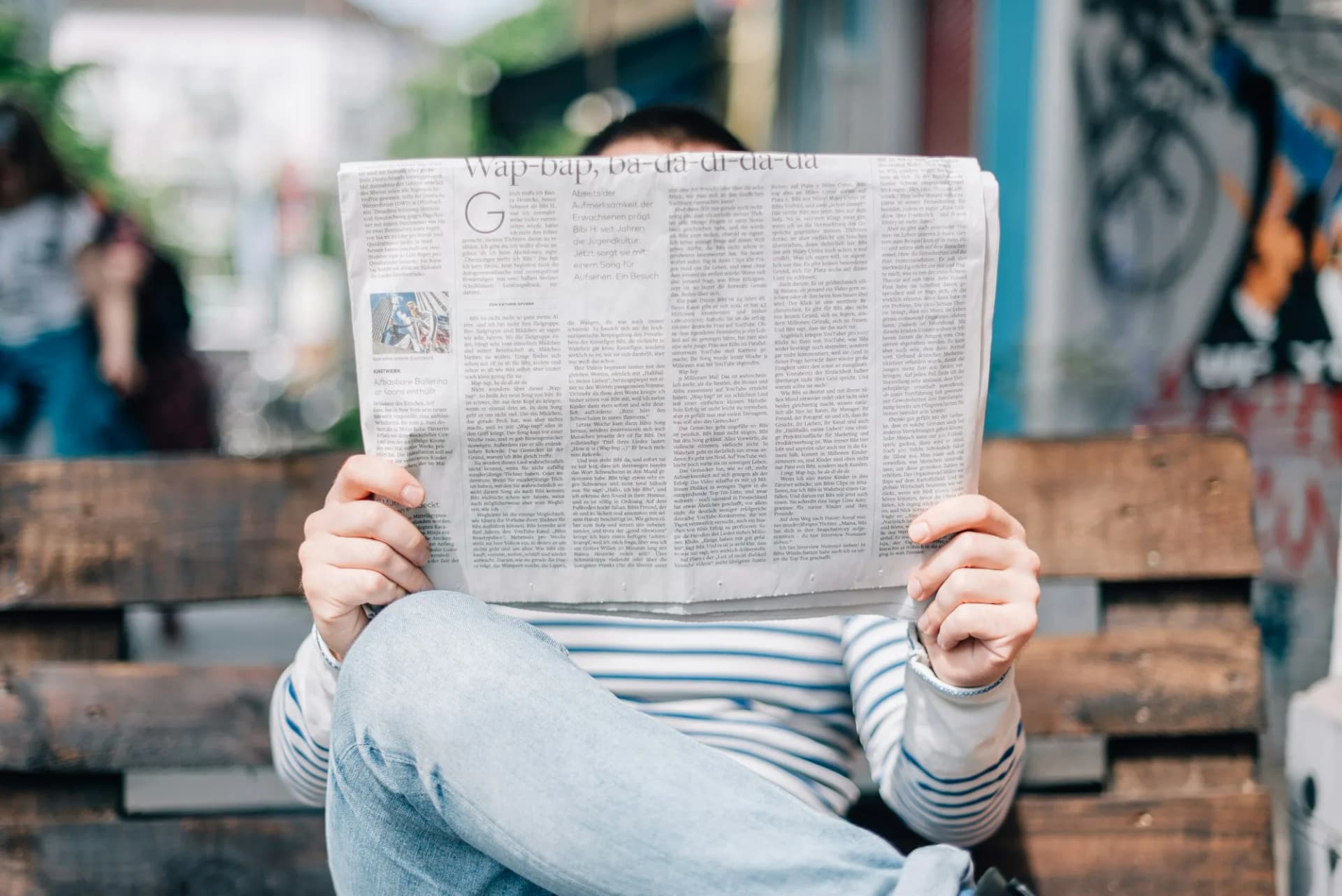 Un lecteur assis sur un banc, le journal grand ouvert devant lui